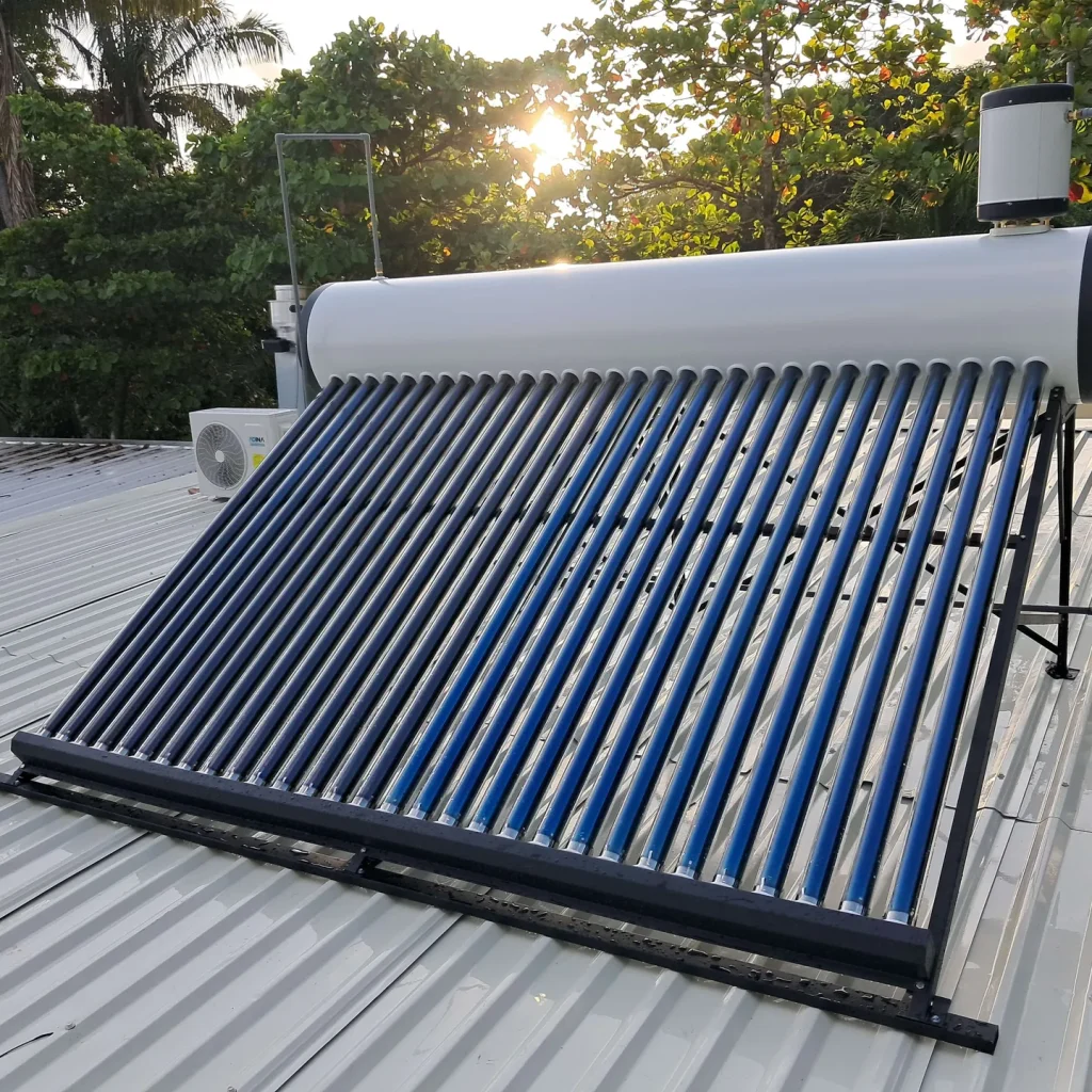 Sistema completo de calentamiento solar con tanque blanco y tubos de vacío azules sobre techo blanco al atardecer.
