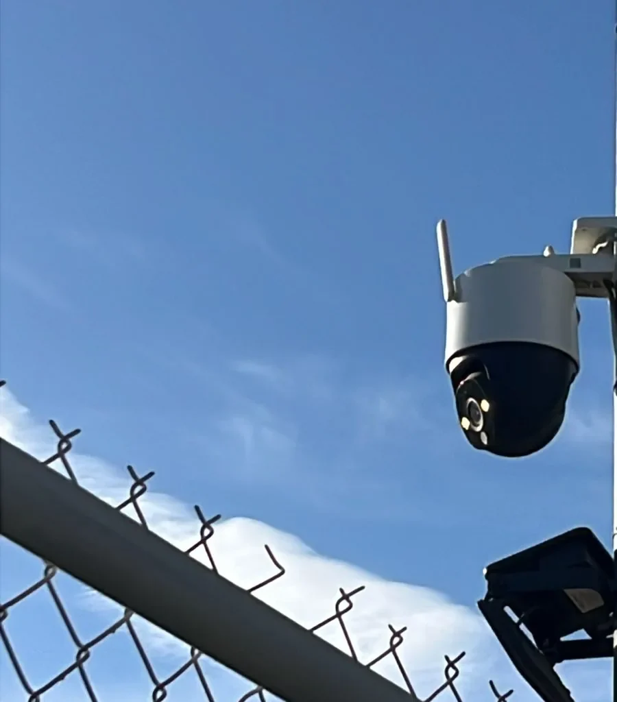 Cámara domo PTZ blanca con antena montada en poste metálico bajo cielo azul despejado.