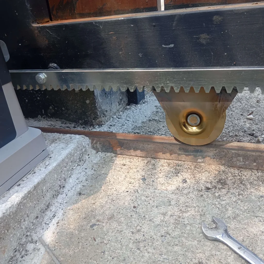 Detalle de instalación: motor corredizo, cremallera dentada y rueda de soporte dorada sobre riel.