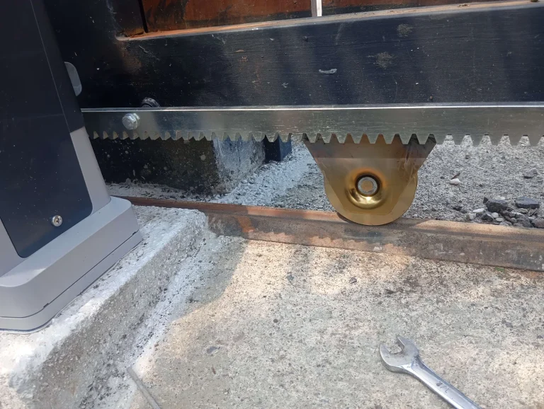 Detalle de instalación: motor corredizo, cremallera dentada y rueda de soporte dorada sobre riel.