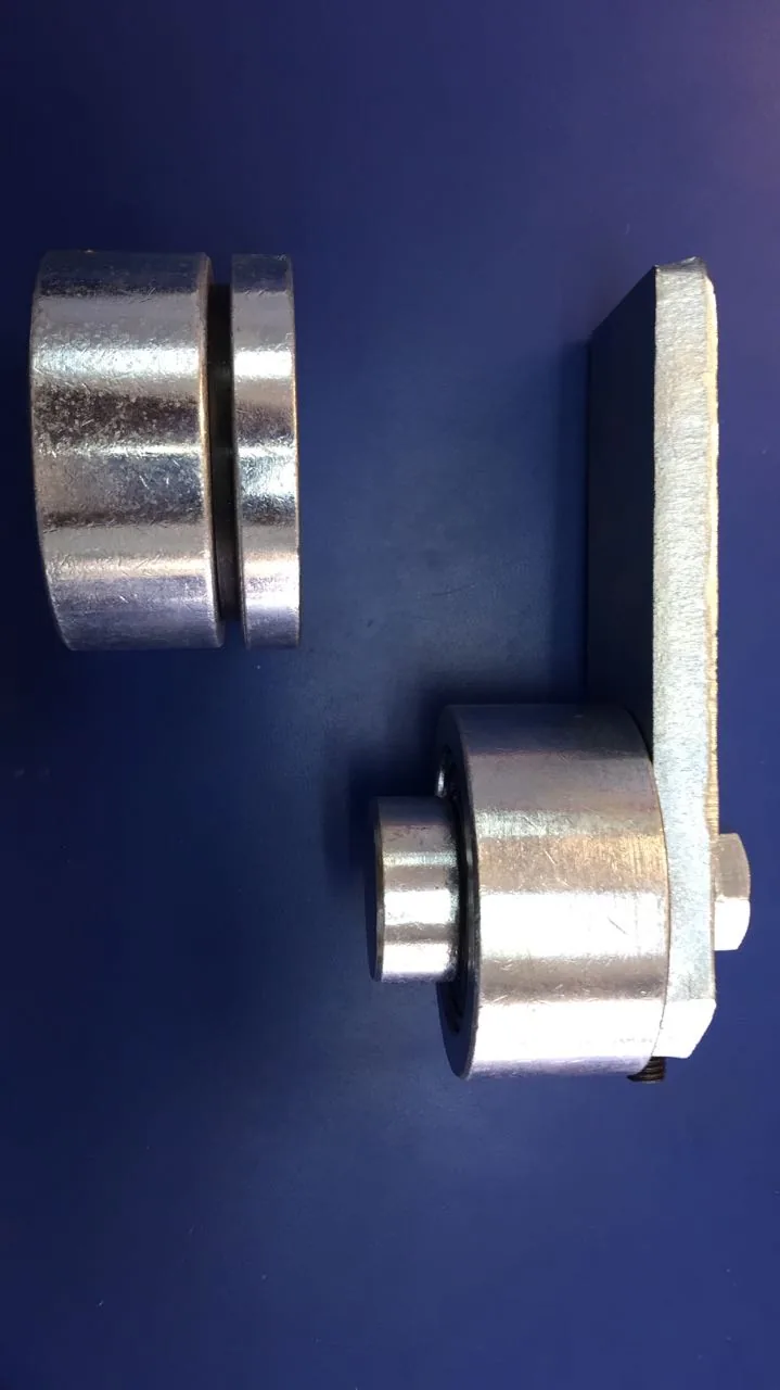 Dos herrajes metálicos galvanizados: rueda con ranura y pivote con placa de montaje para portones.