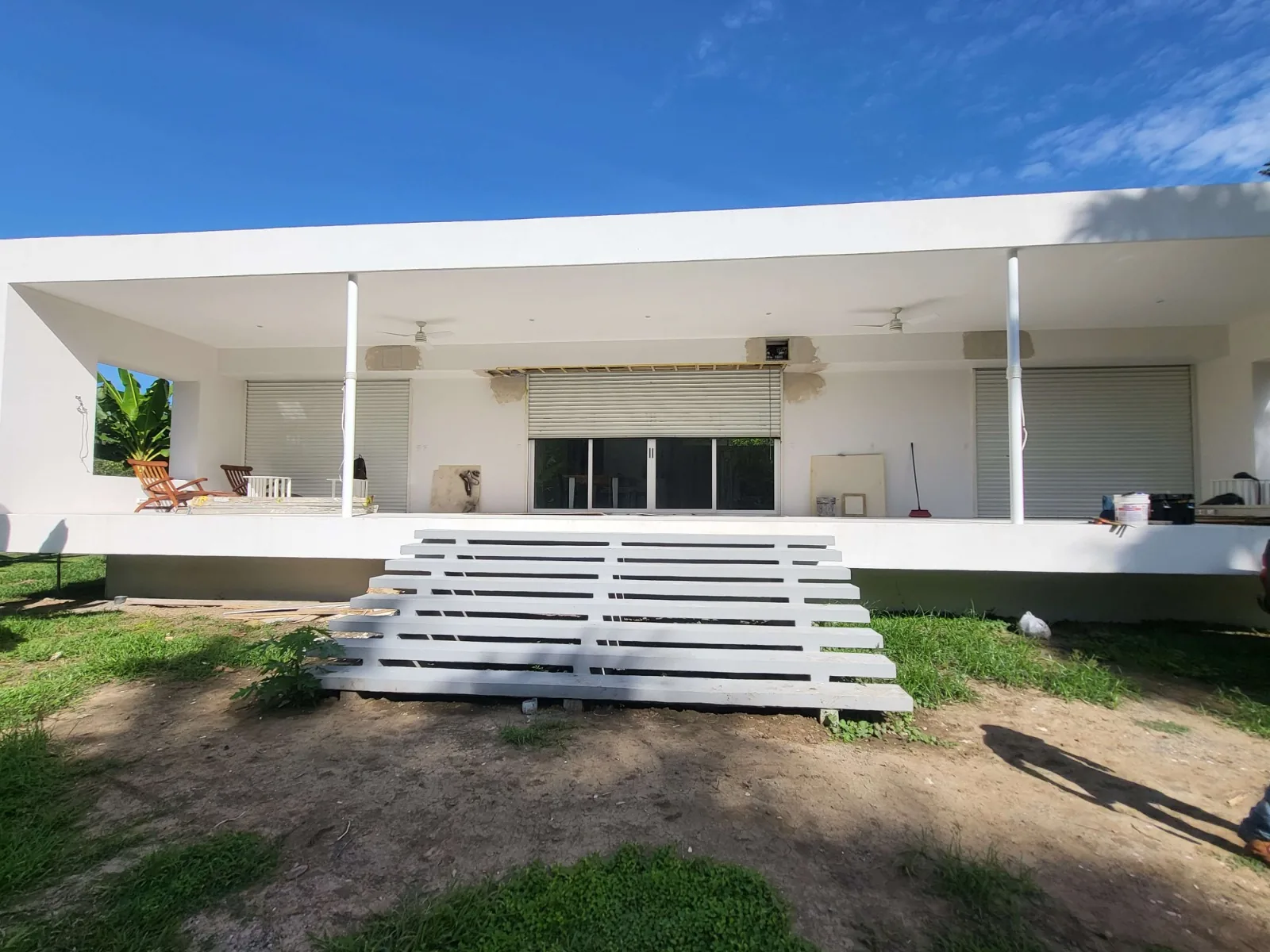 Edificio blanco con tres cortinas metálicas enrollables: una parcialmente abierta sobre puerta de vidrio y dos cerradas.